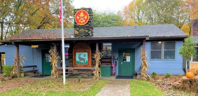 A Scout camp office building in autumn, with a flagpole and corn stalks by the door