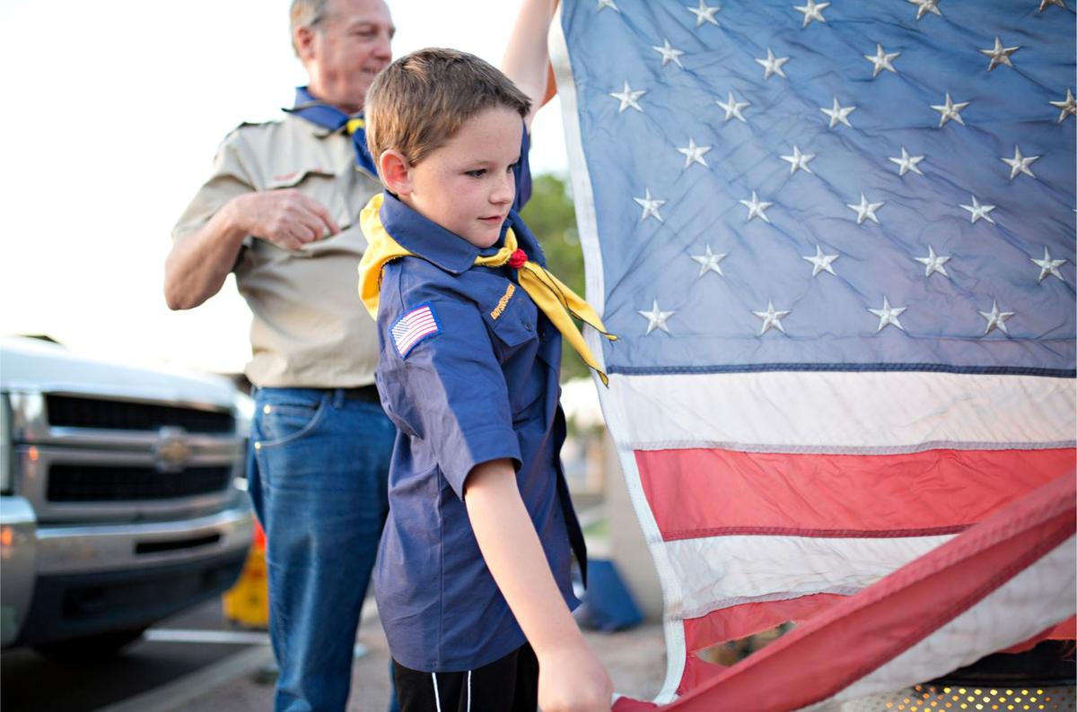 A young Cub Scout helping an adult leader raise the American flag
