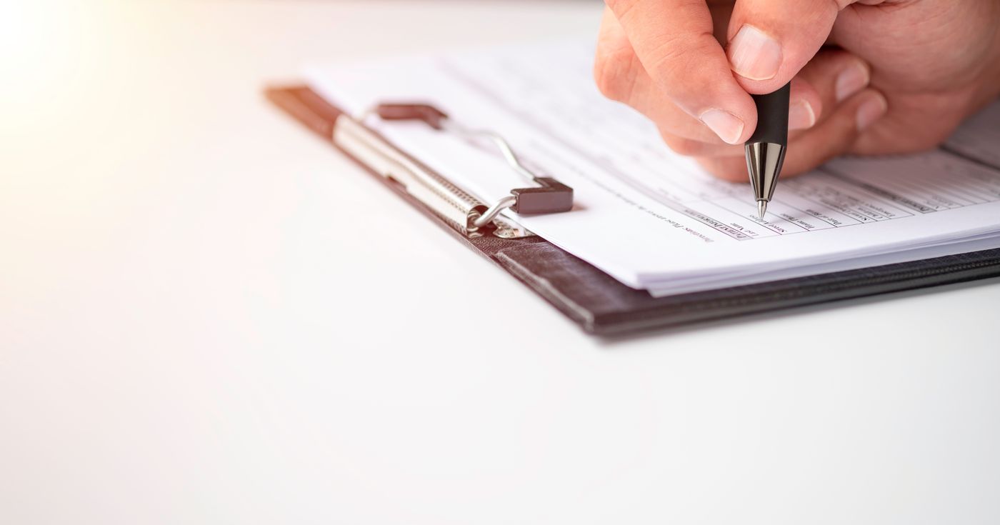 A hand filling out a form on a clipboard