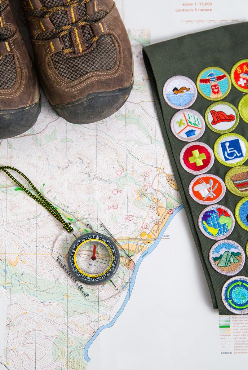 Hiking boots, a compass, and a merit badge sash on a trail map